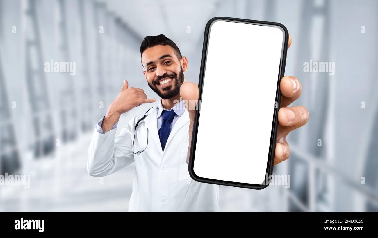 Middle eastern male doctor showing blank smartphone and making call me gesture Stock Photo