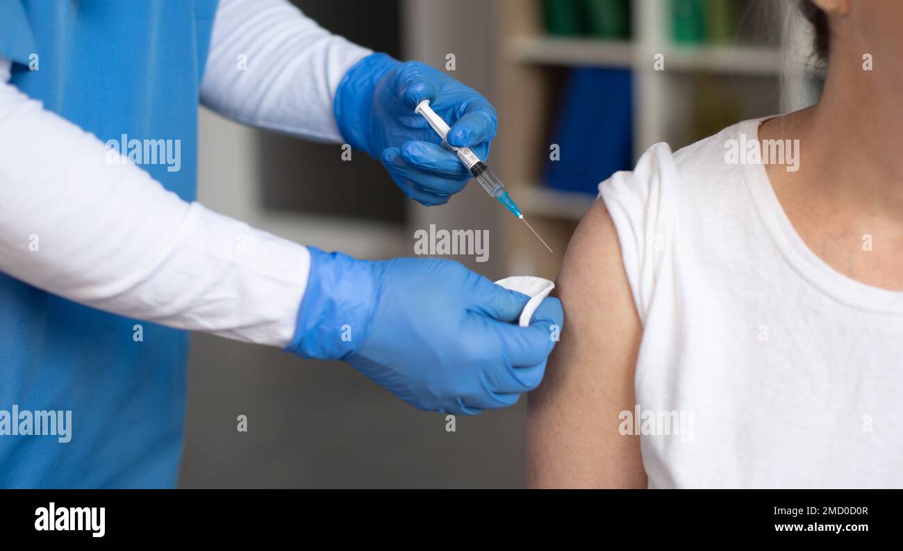 Hands of doctor in protective gloves make injection with syringe of old caucasian female patient in clinic Stock Photo
