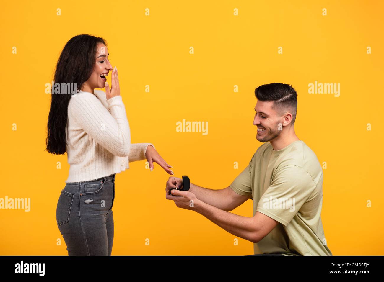 Glad millennial arab man kneeling, holding ring box with jewelry, proposing to surprised lady Stock Photo