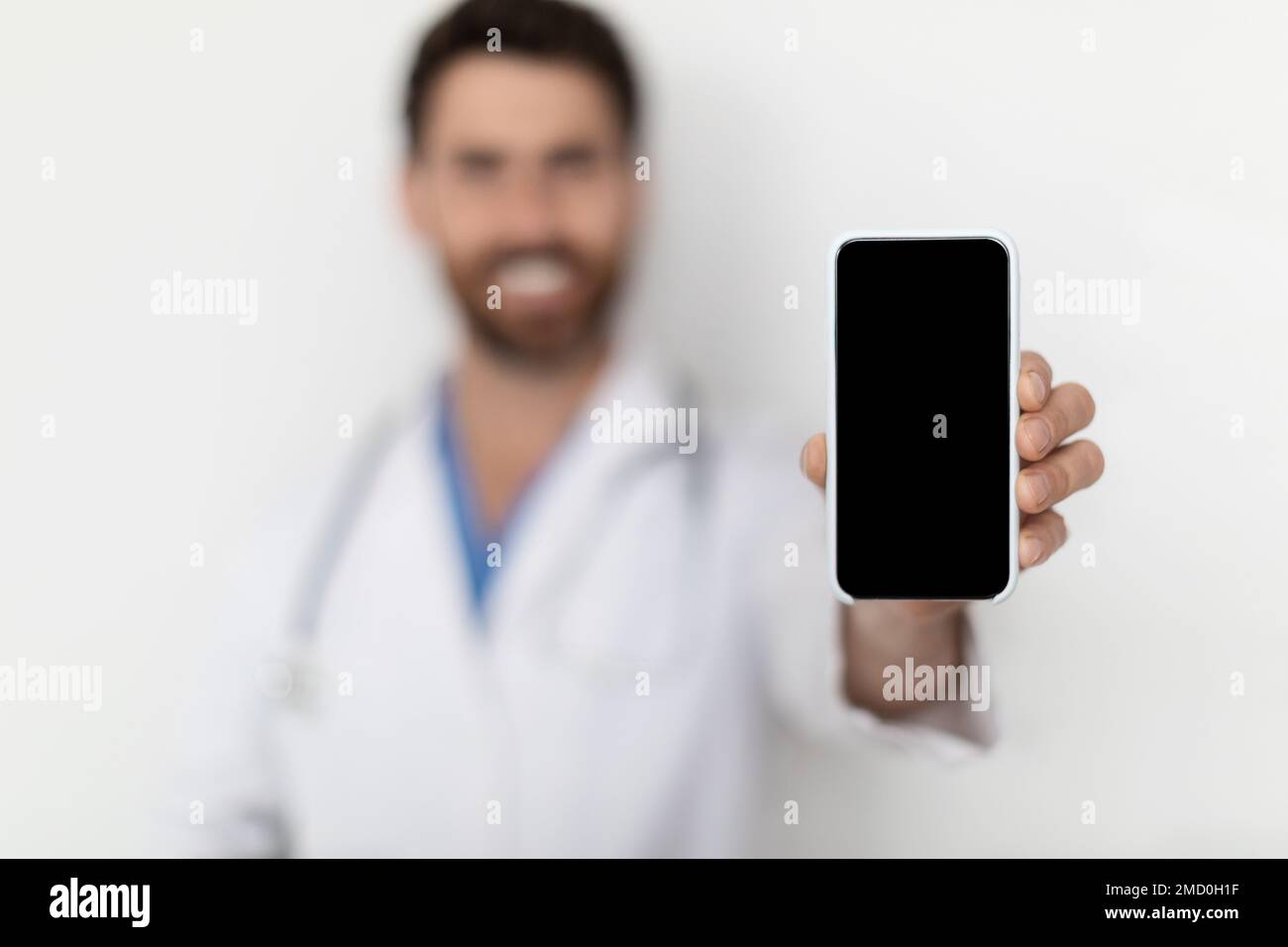 Check This. Smiling Male Doctor Demonstrating Blank Smartphone At Camera Stock Photo