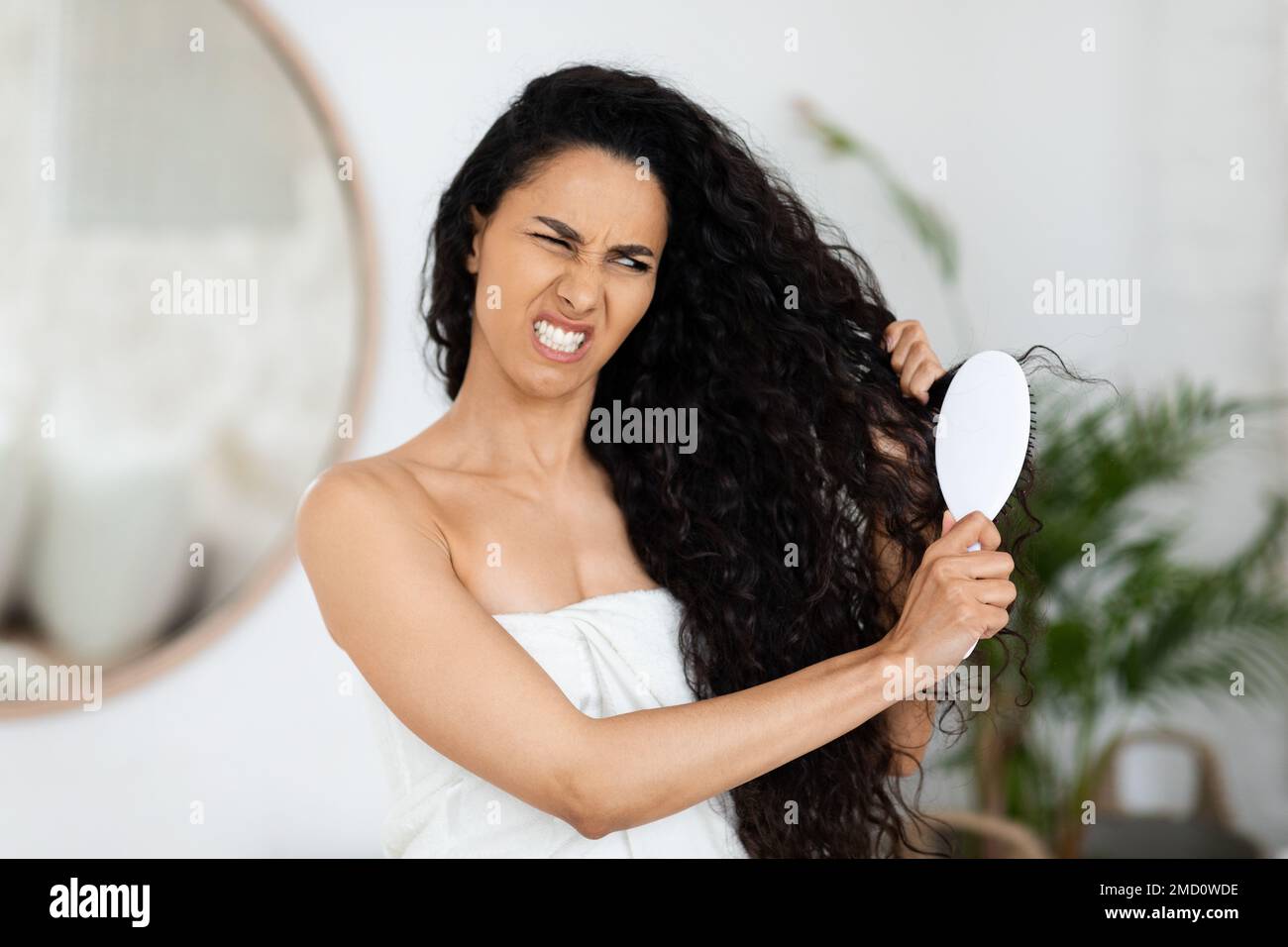 Unhappy sad arab millennial curly woman in towel combing her dry
