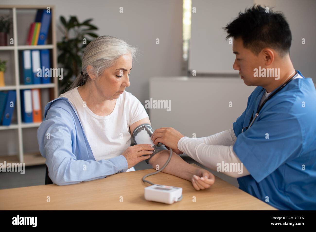 Serious mature korean doctor measures pressure with tonometer of old european woman patient in clinic Stock Photo