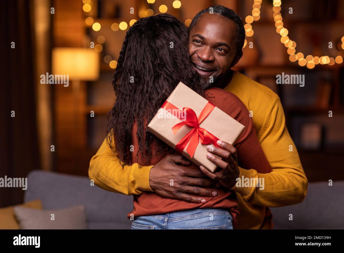 Thankful happy handsome black man holding present and hugging wife ...