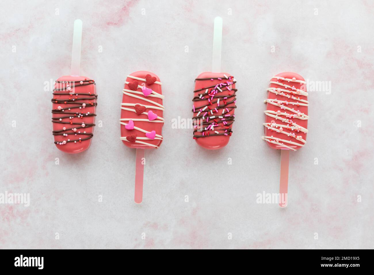 Alternating up and down facing Valentine cakesicles on a pink marble surface. Stock Photo