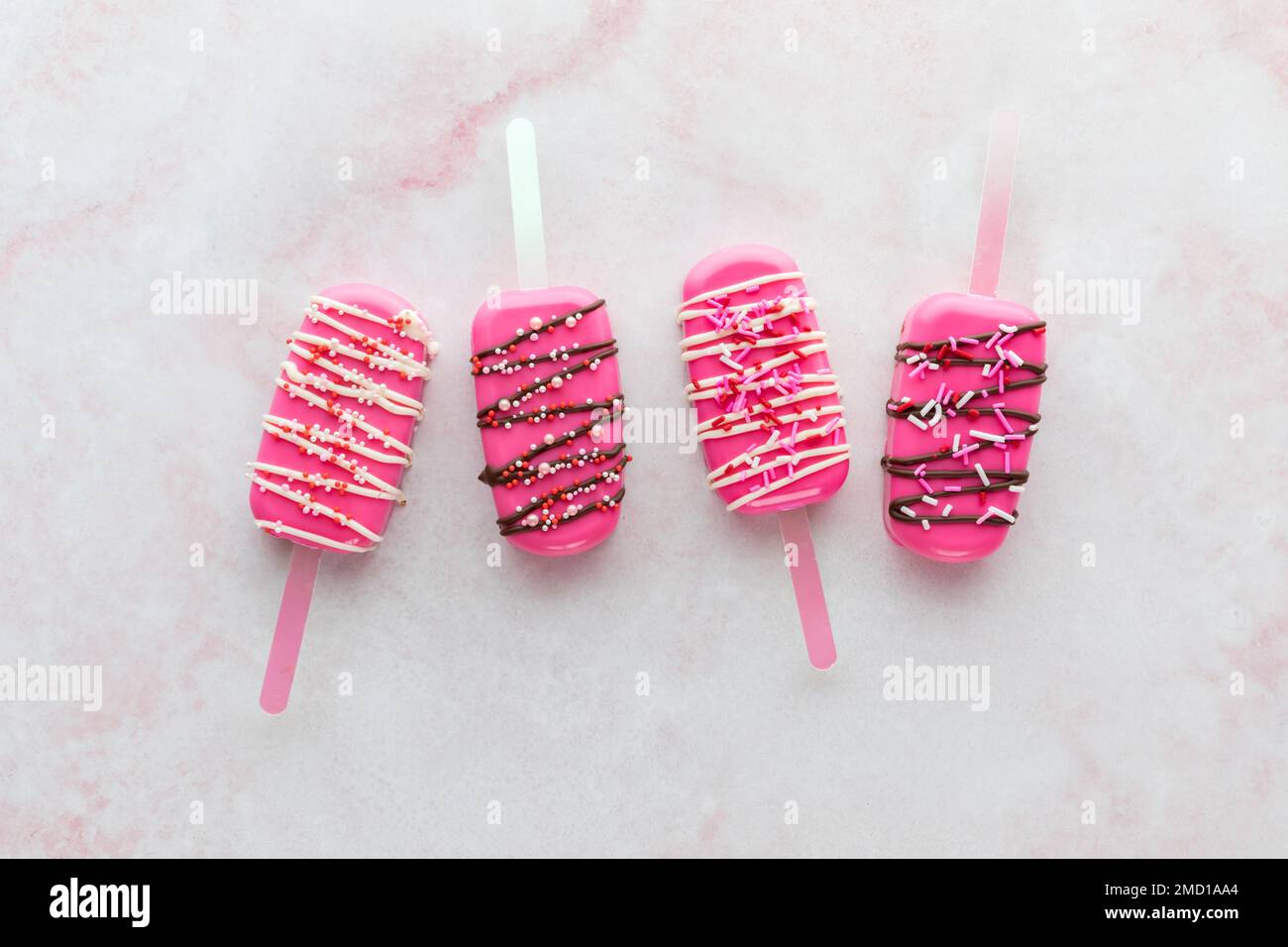 Homemade decorated cakesicles for Valentine's Day, on a pink marble surface. Stock Photo