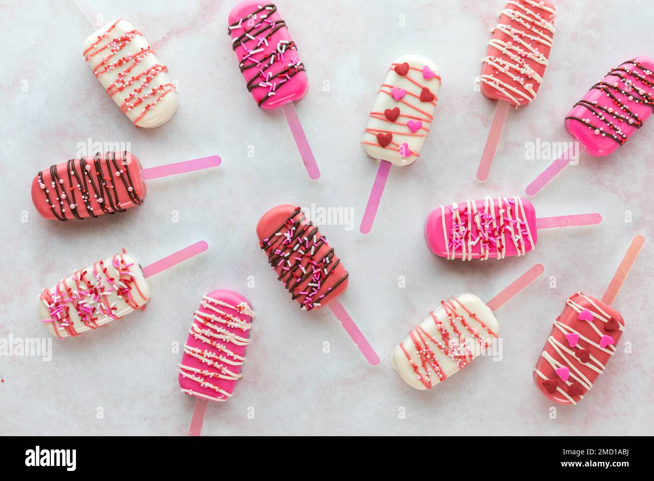 Several Valentine cakesicles scattered on a pink marble surface. Stock Photo