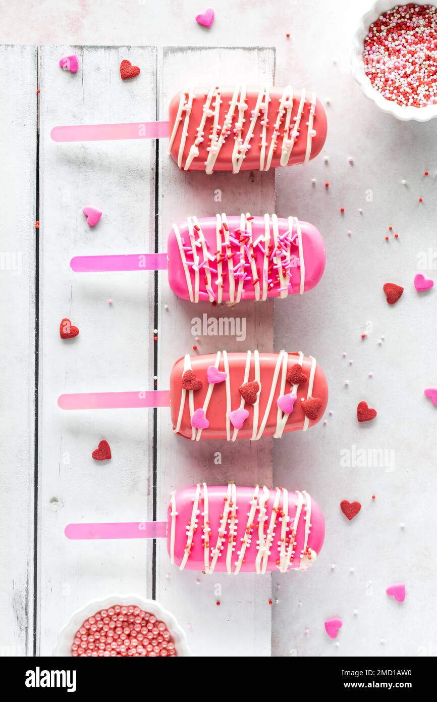 Valentine's Day cakesicles on a rustic wooden board with sprinkles all around. Stock Photo