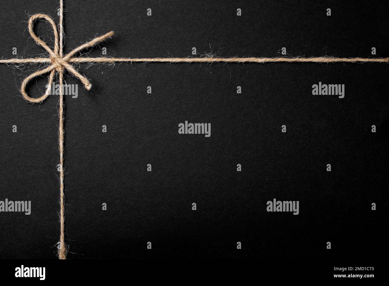 Jute string bow and framing lines on black paper texture, close up ...