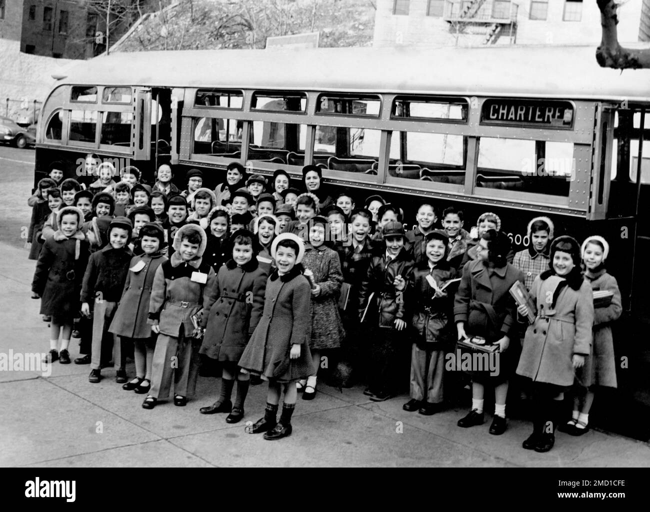 A vintage photograph of a large group of boys and girls in NY standing in front of their school bus, circa 1952. Stock Photo