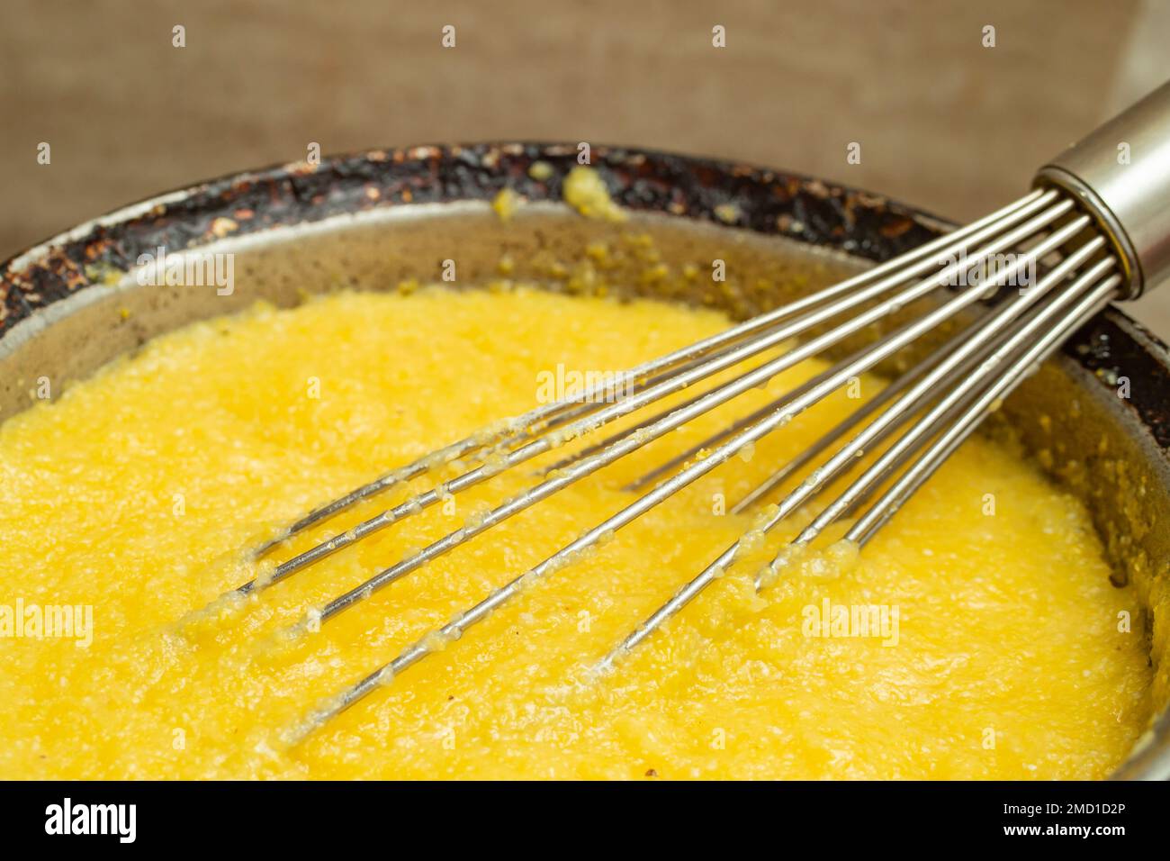 Boiling corn flour in a cast iron pot, making mamaliga, traditional romanian food, and mixing with a stainless steel whisk, soft focus close up Stock Photo