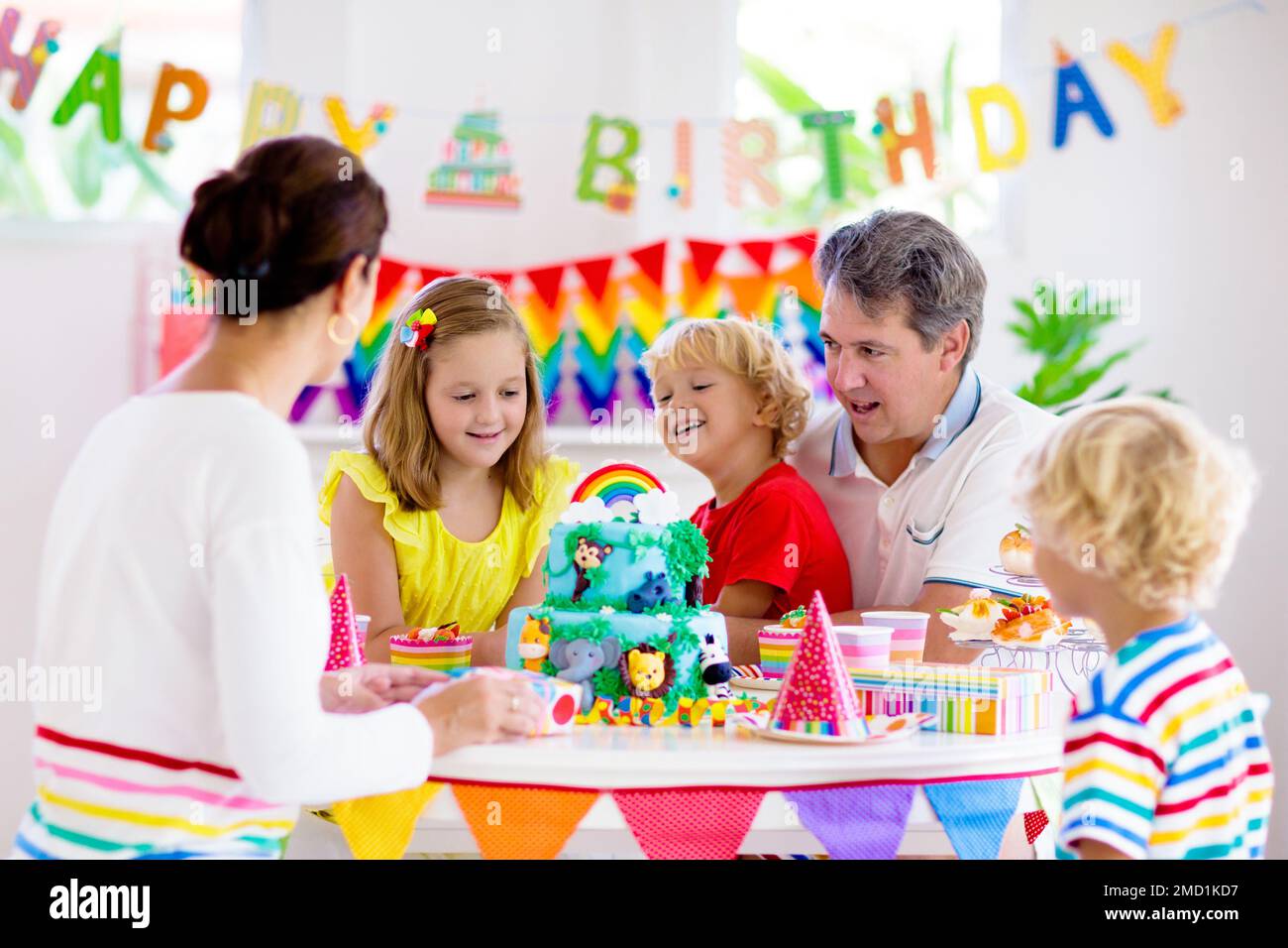 Kids birthday party. Child blowing candles on cake and opening presents