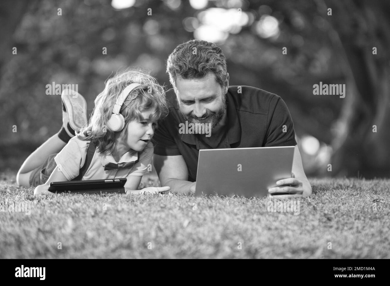 Dad And Son Use Laptop For Video Call Or Lesson Listen Music In Headphones In Park Education