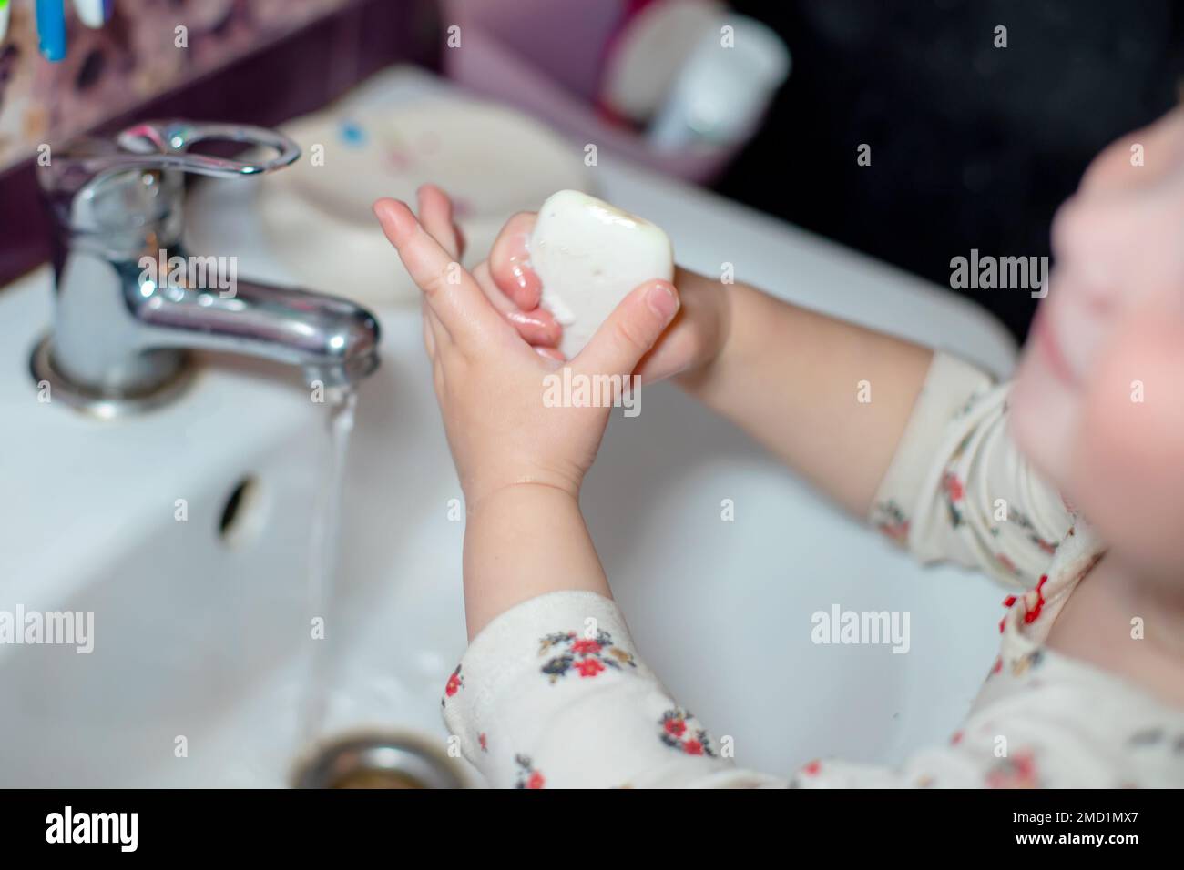 little girl washing hands with white soap in bathroom. child near white