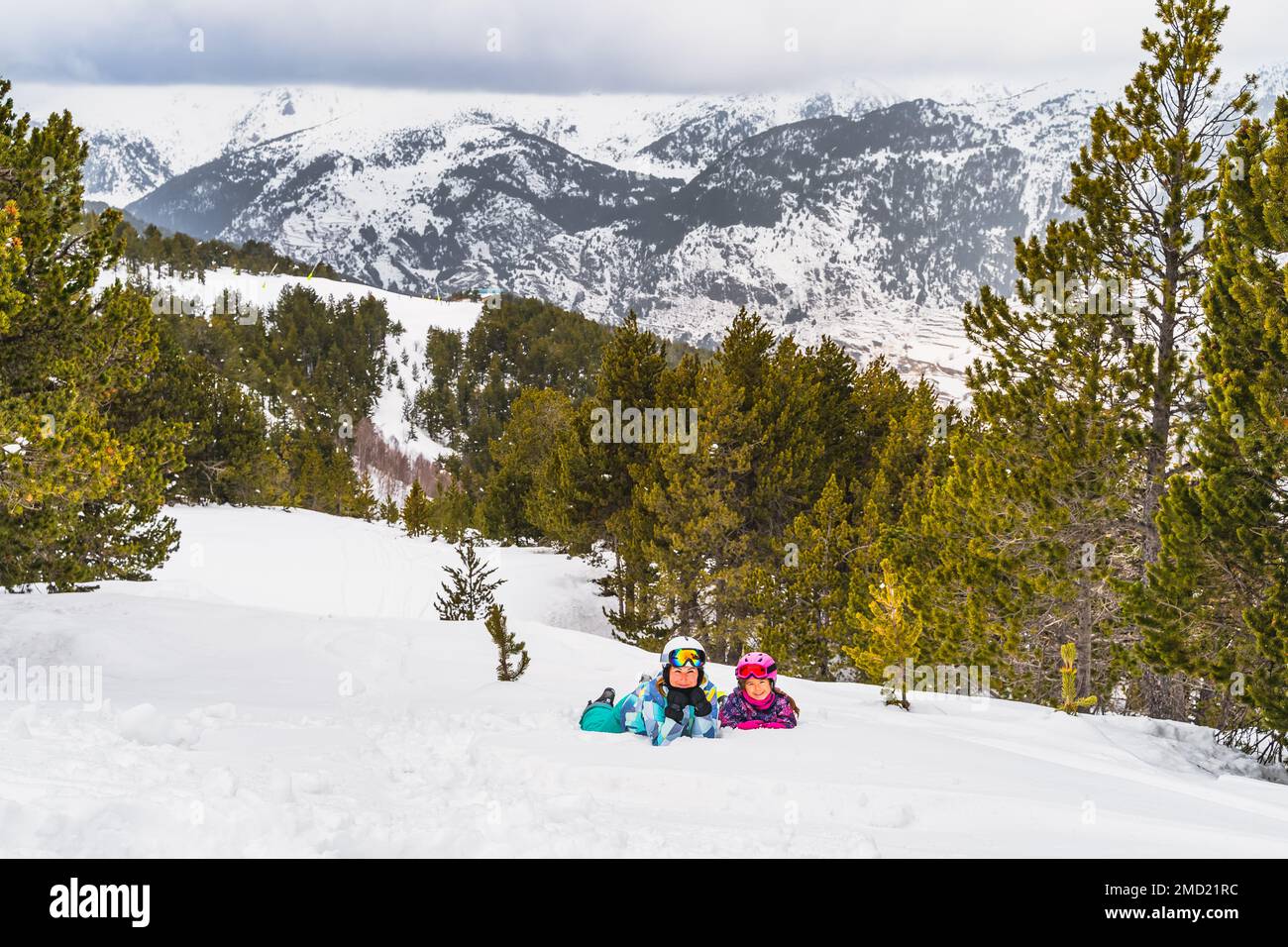 Mother and daughter lying down on a snow smiling and looking at camera,  forest and mountain range in background. Winter ski holidays, Andorra  Pyrenees Stock Photo - Alamy