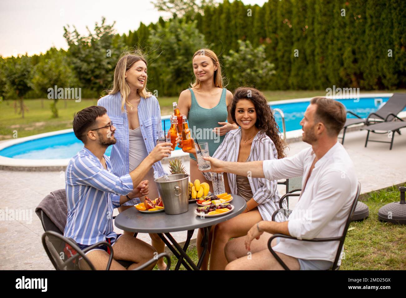 Group of happy young people cheering with cider by the pool in the garden Stock Photo