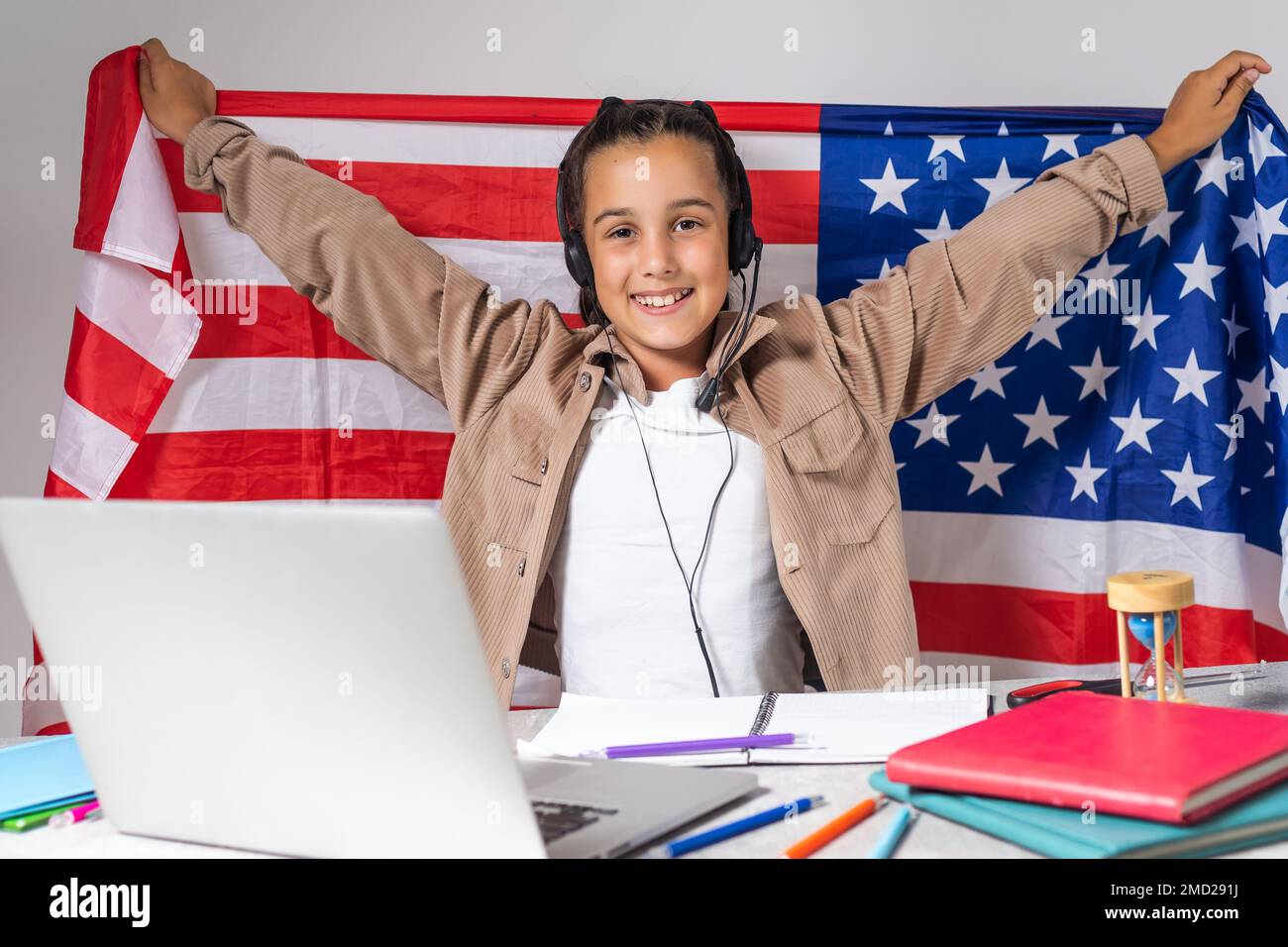 beautiful pupil sitting at desk and study online with laptop against background with USA flag. Stock Photo