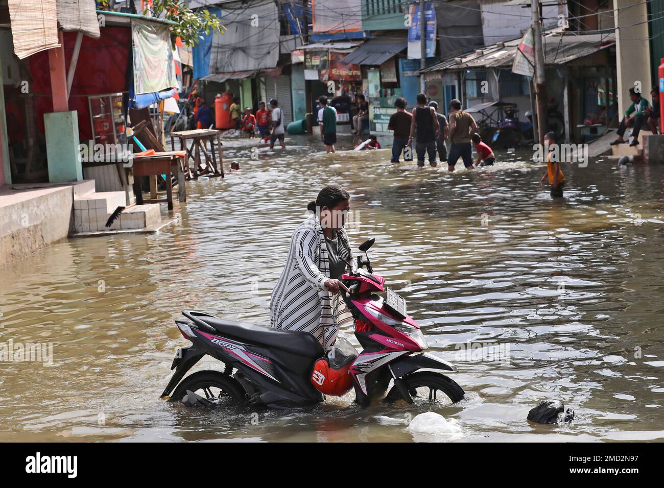 A woman pushes her motorbike through the water during a tidal flood in Jakarta, Indonesia