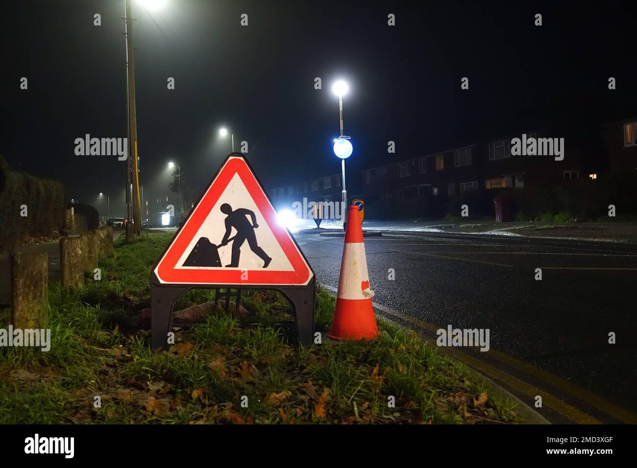 A triangular roadworks sign and traffic cone at the side of a road at night to worn motorists of roadworks ahead, Stock Photo