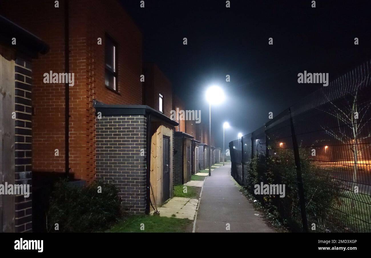 A footpath at night lit with street lights with the doorways to modern town houses on one side and a black metal fence on the other. Stock Photo
