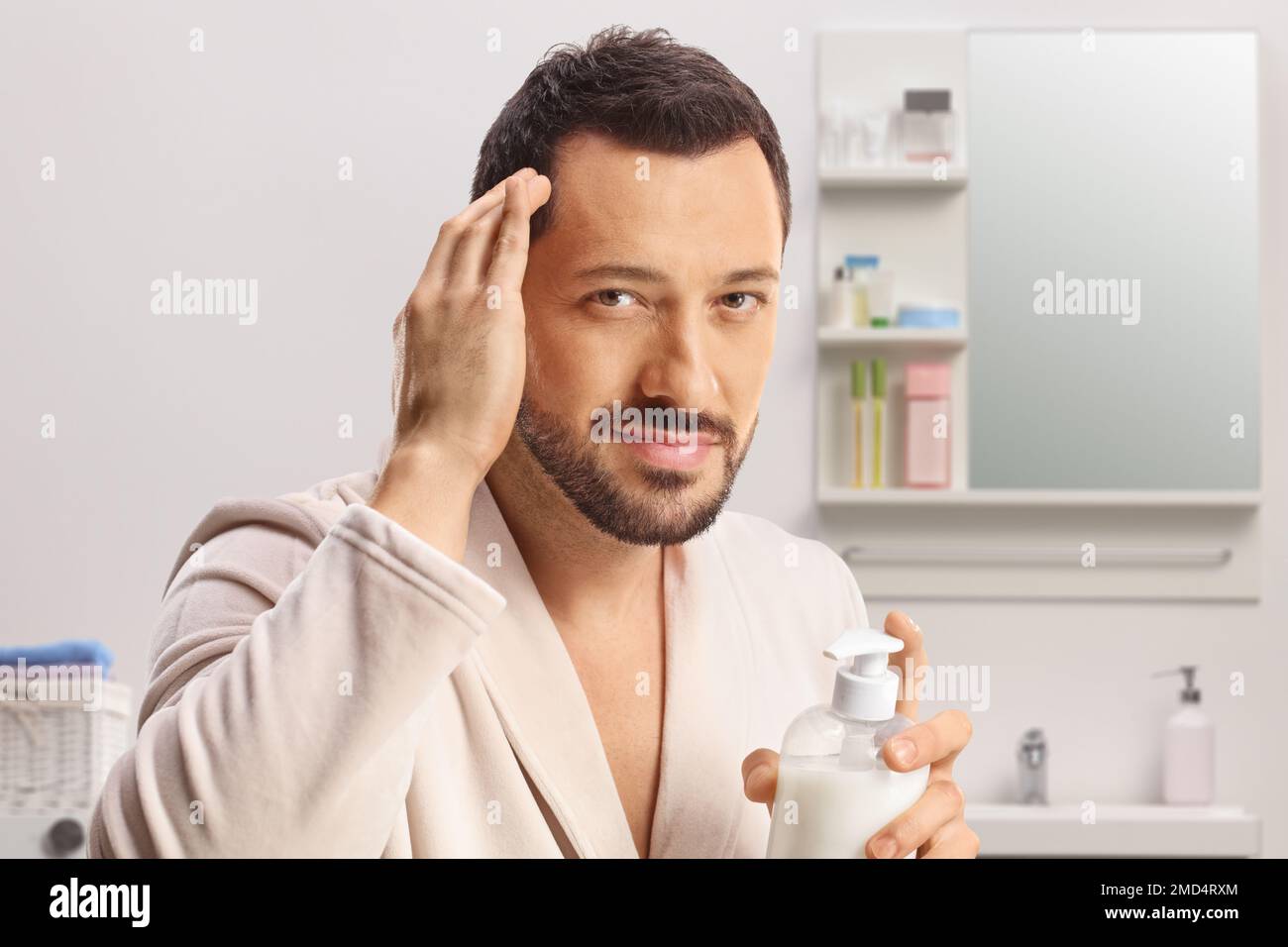 Young man in a bathrobe putting on a hair conditioner inside a bathroom Stock Photo