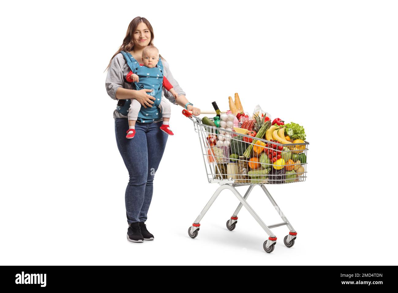 Mother with a baby in a carrier and a shopping cart full of food isolated on white background Stock Photo