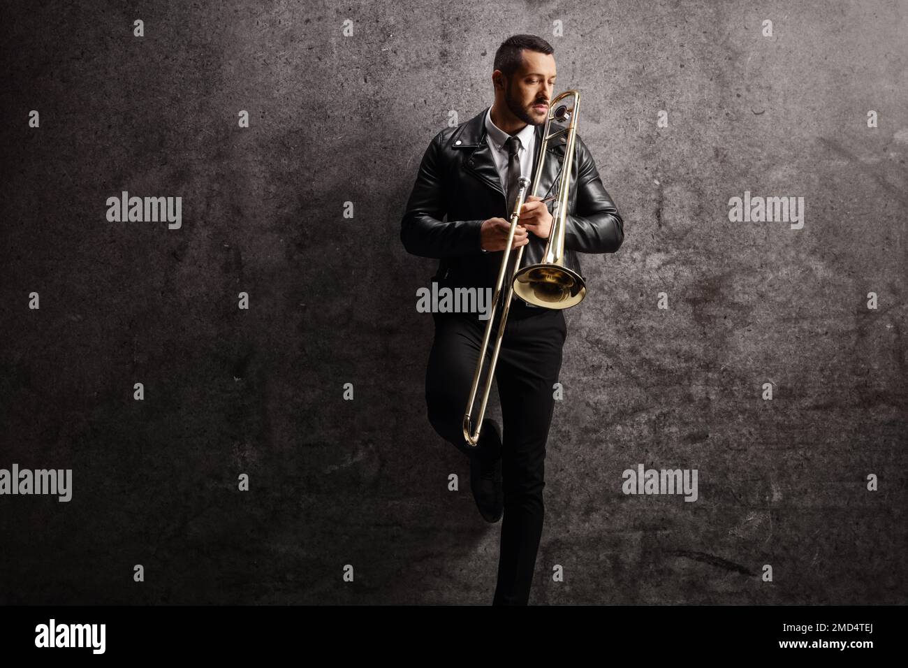 Young man holding a trombone and standing against a gray wall Stock Photo
