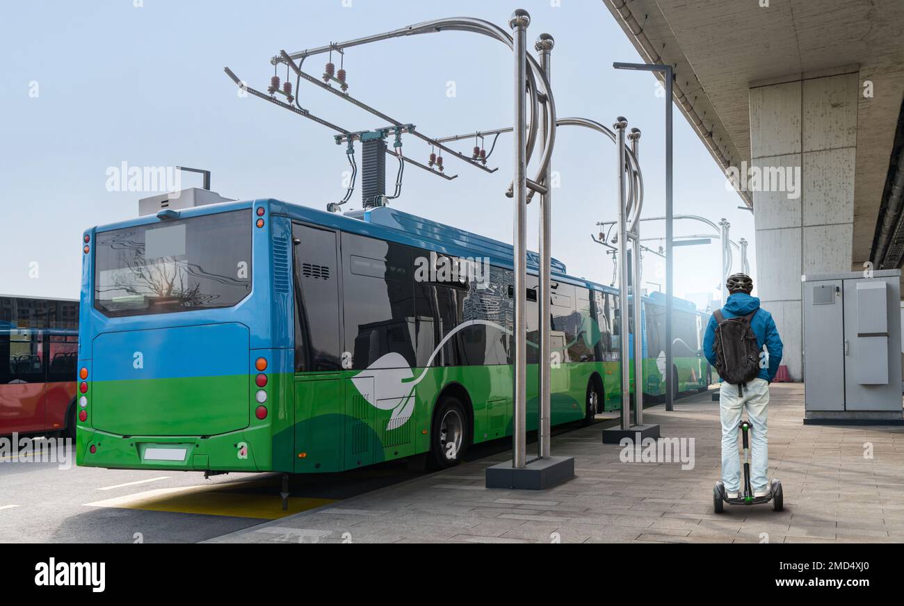 Man on electric scooter next to electric bus at a stop is charged by pantograph. Stock Photo