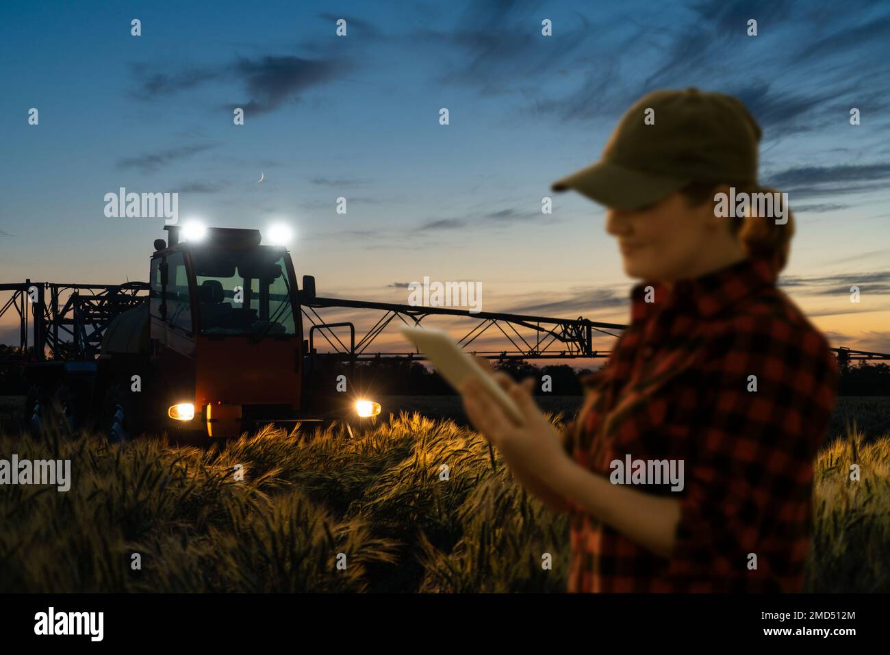 Farmer controls sprayer with a tablet at night. Smart farming and precision agriculture Stock Photo
