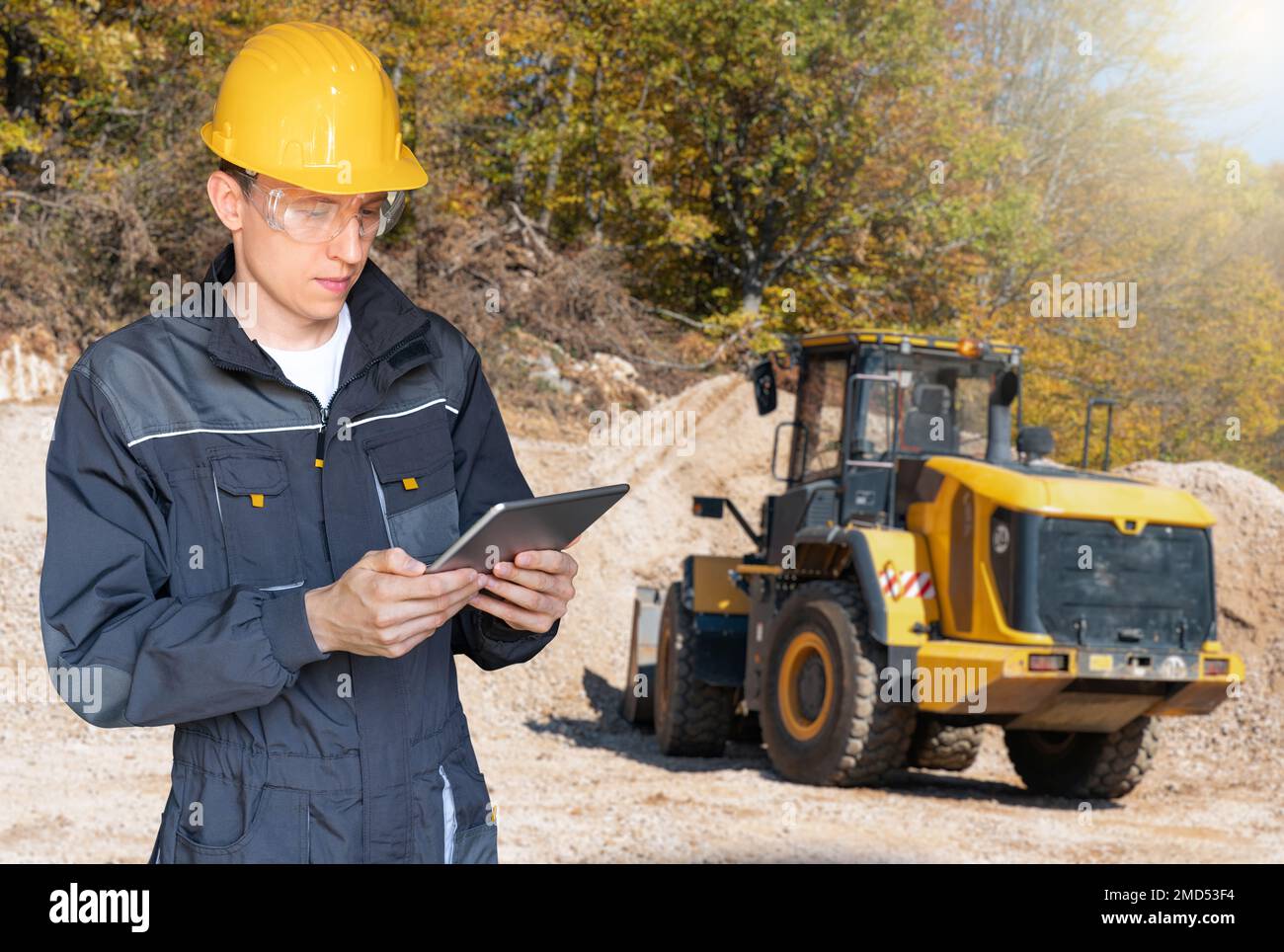 Engineer in a helmet with a digital tablet on the background of construction machine Stock Photo