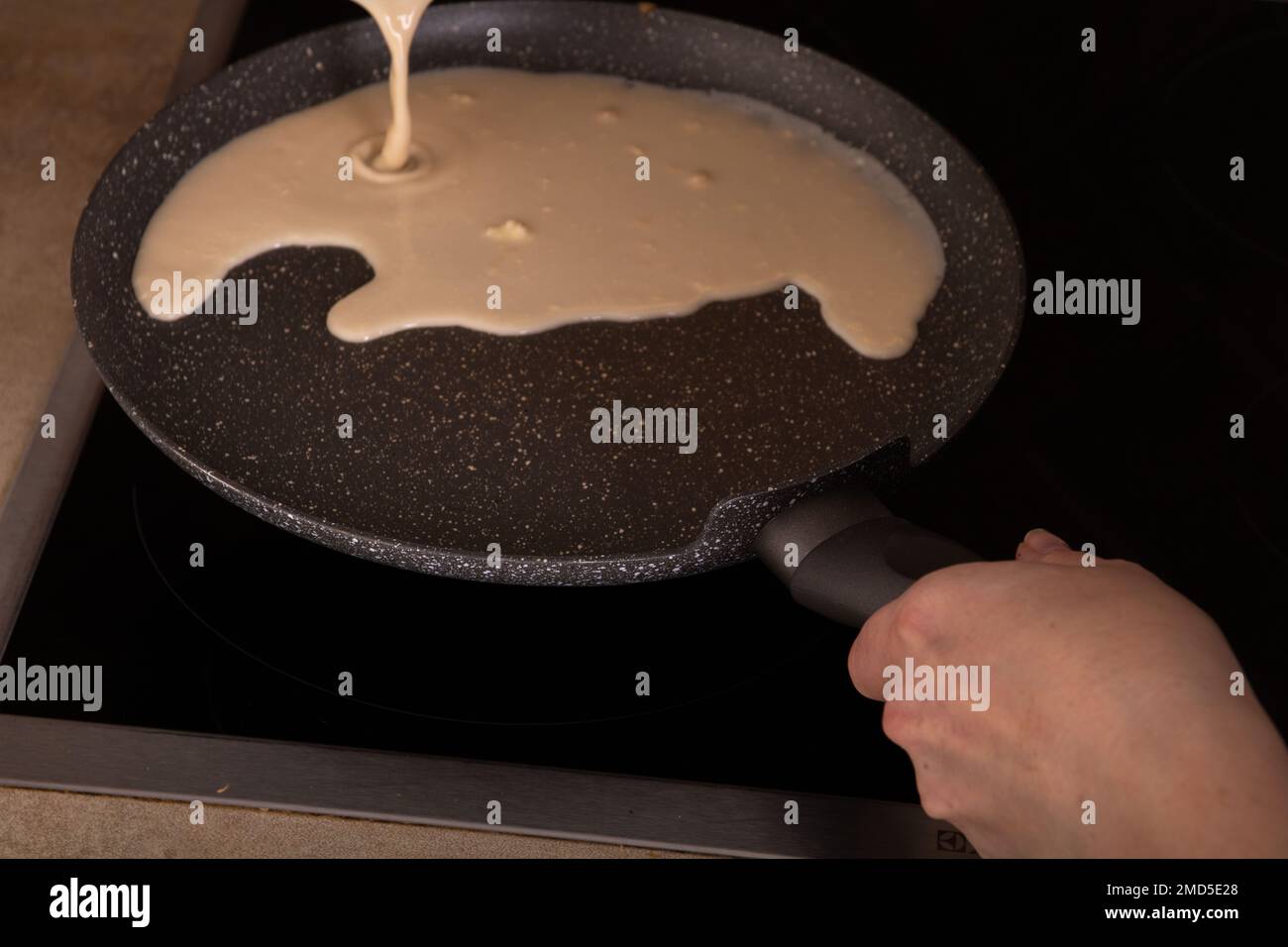 photo of liquid batter pouring onto a pancake pan, with a hand holding