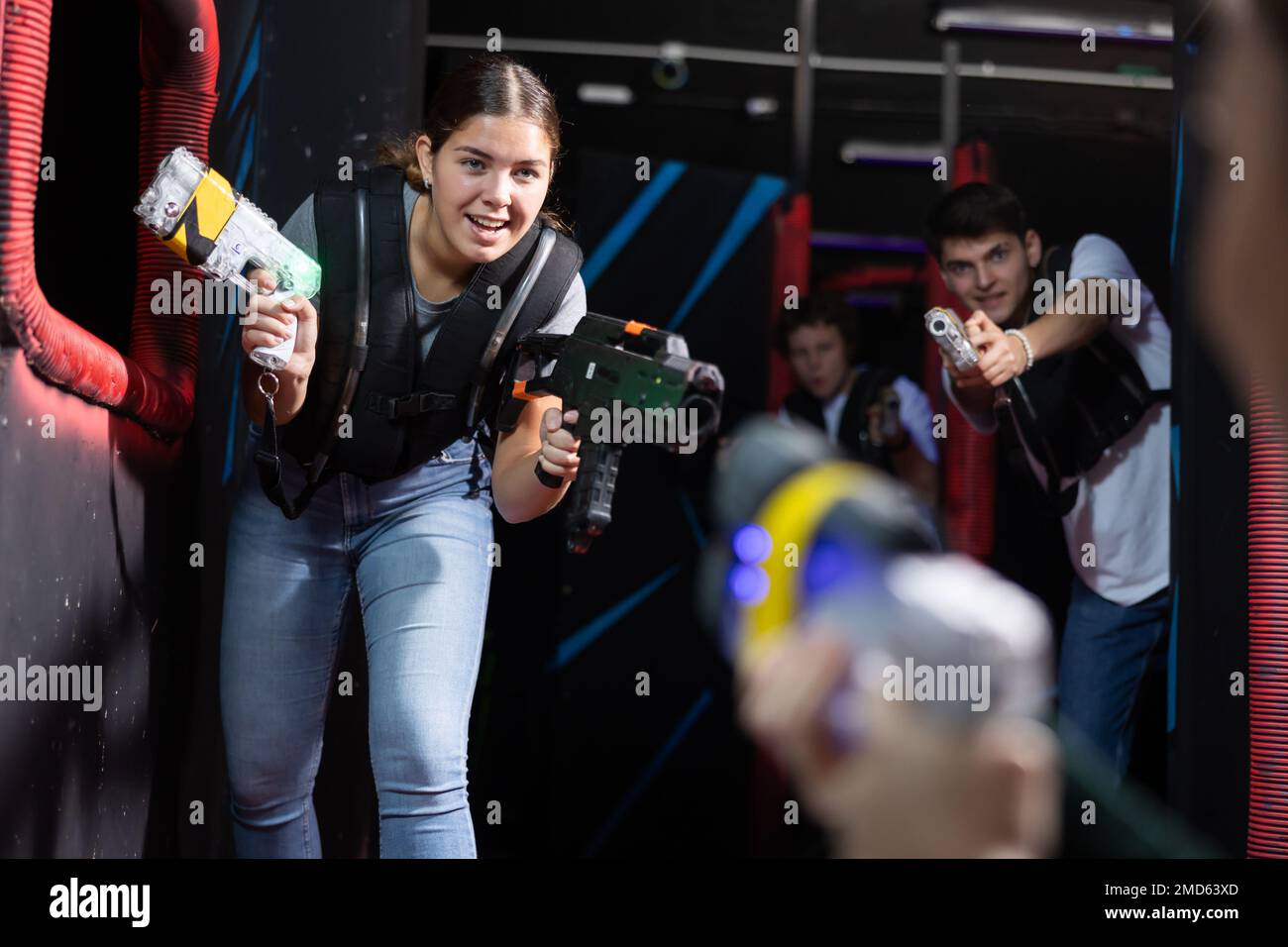 Positive girl holding laser pistol playing laser tag game with friends
