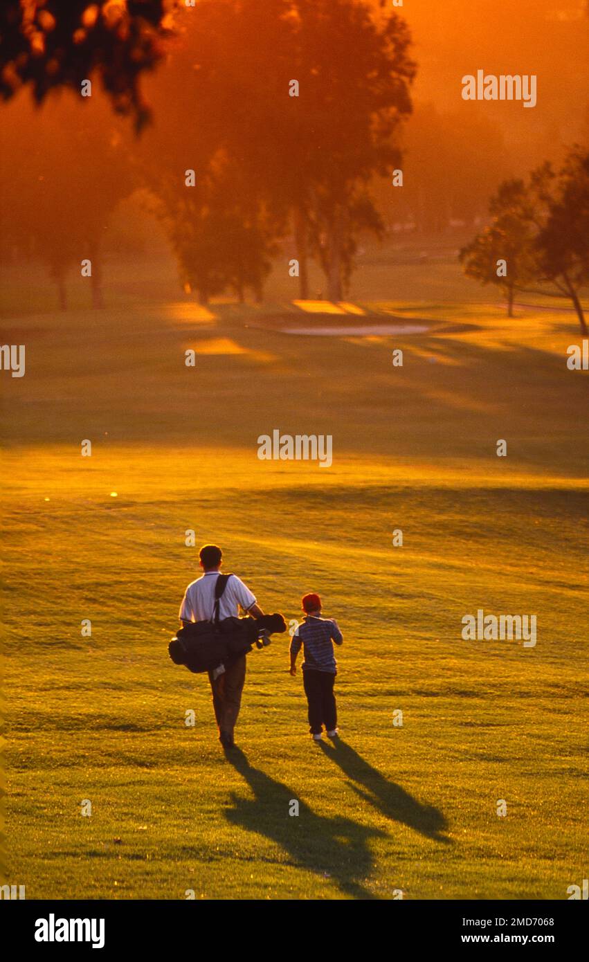 Longshot of a father with his young son walking the golf course at sunset Stock Photo