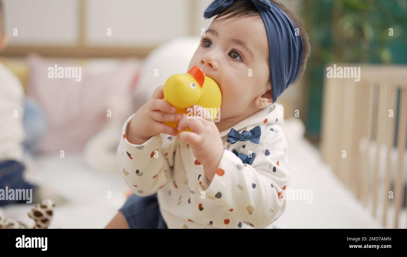 Adorable toddler sitting on bed bitting duck toy at bedroom Stock Photo ...