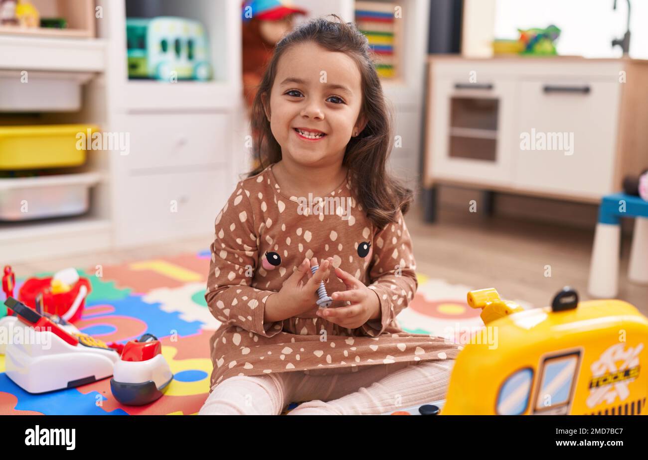 Adorable hispanic girl sitting on floor playing with mechanic toy at ...