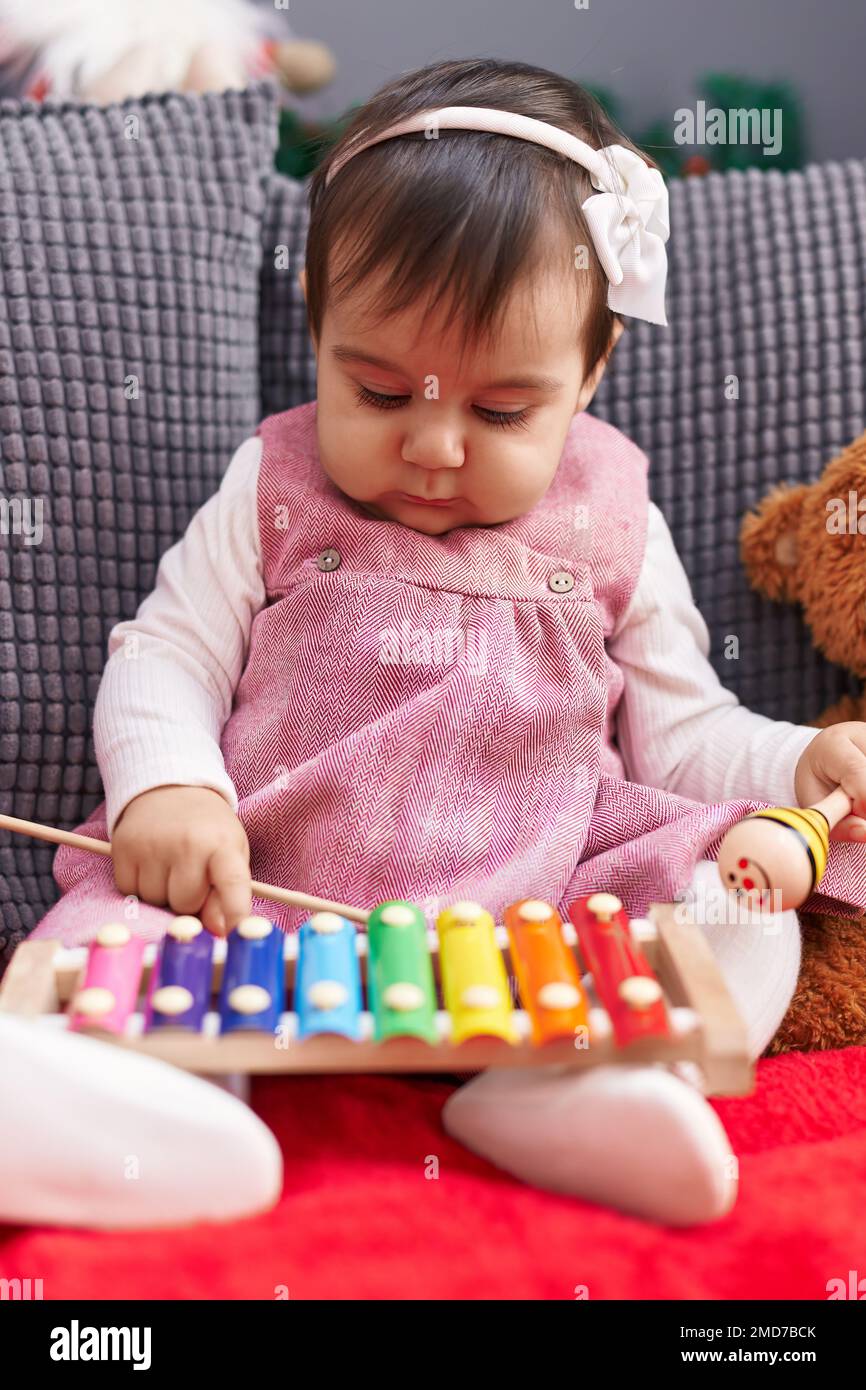 Adorable hispanic baby sitting on sofa playing xylophone and maraca at ...