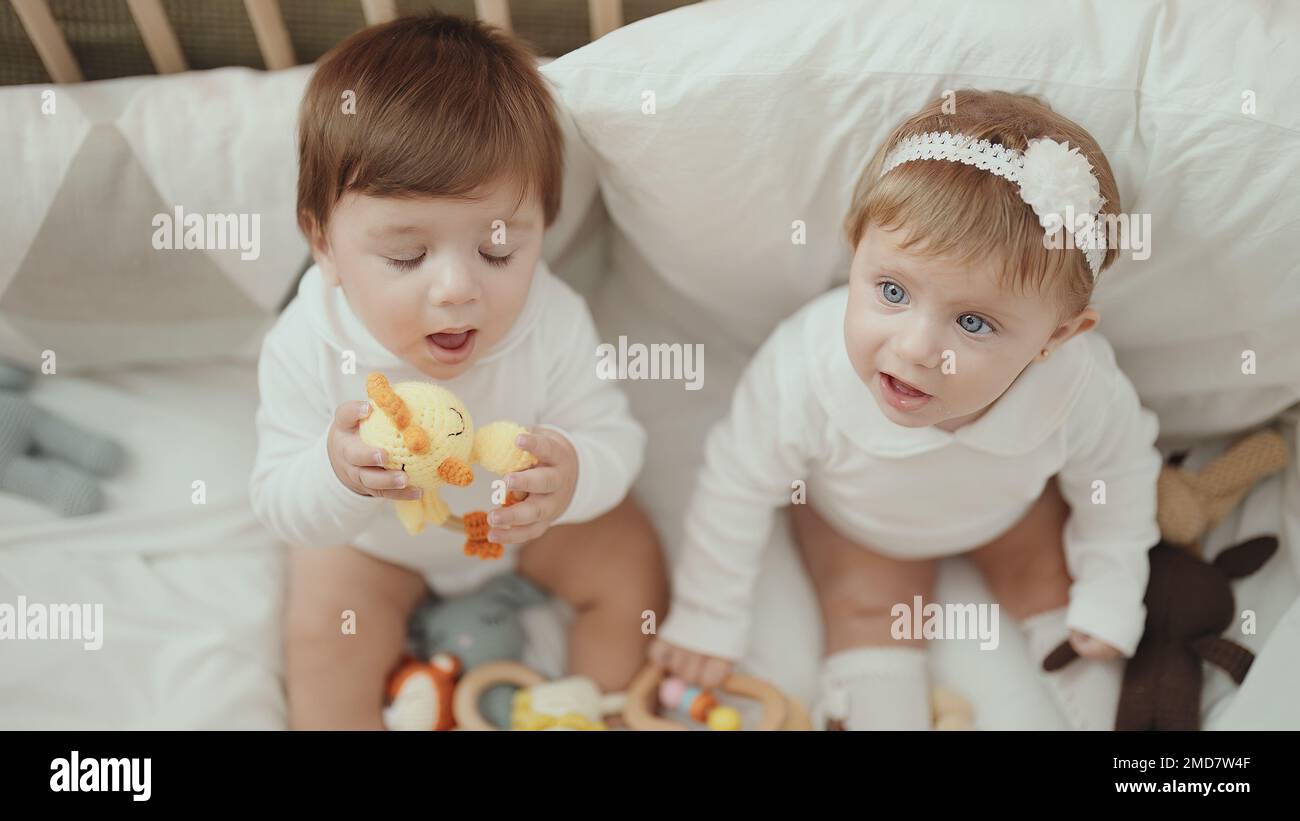 Two adorable babies holding toy sitting on cradle at bedroom Stock ...