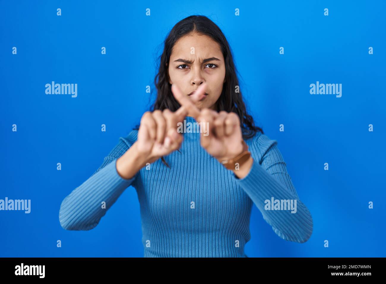 Young brazilian woman standing over blue isolated background rejection ...