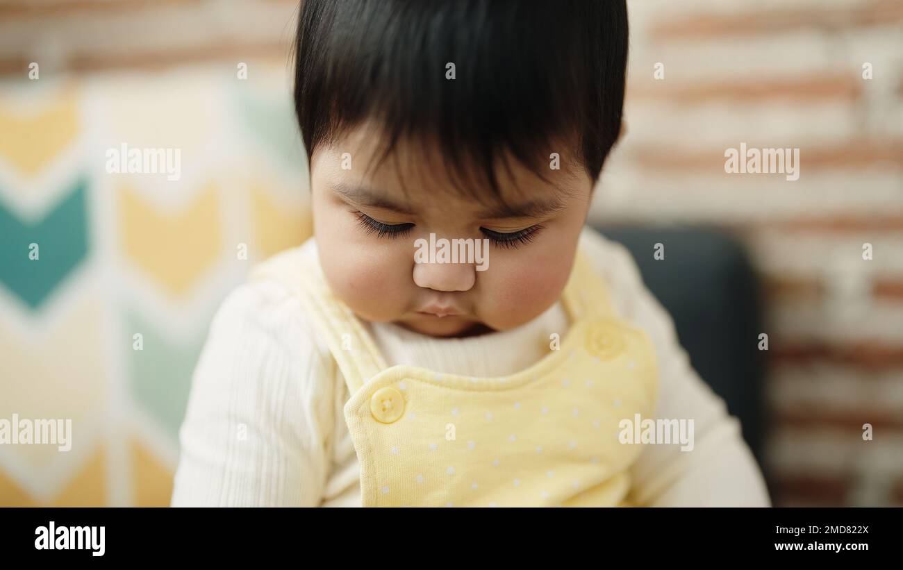Adorable hispanic baby sitting on sofa with relaxed expression at home ...