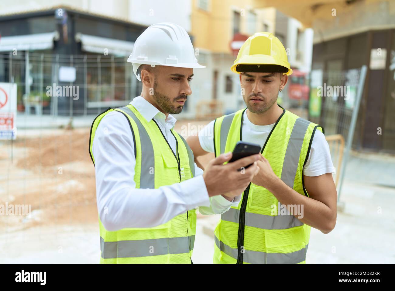 Two hispanic men architects using smartphone standing at street Stock Photo