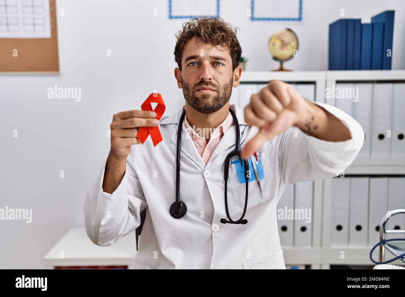 Young hispanic doctor man holding support red ribbon at medical clinic ...