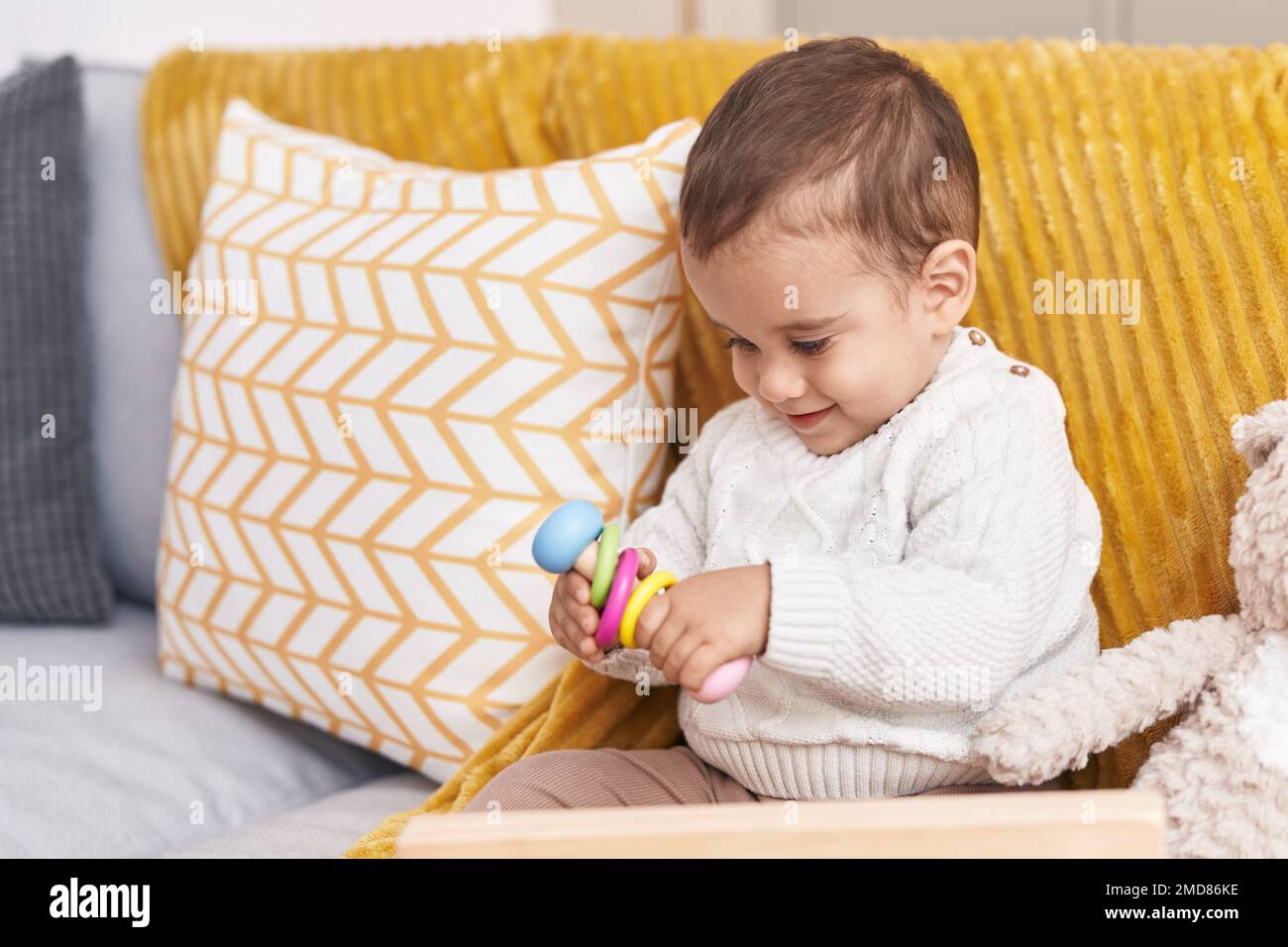 Adorable hispanic toddler playing with toy sitting on sofa at home ...