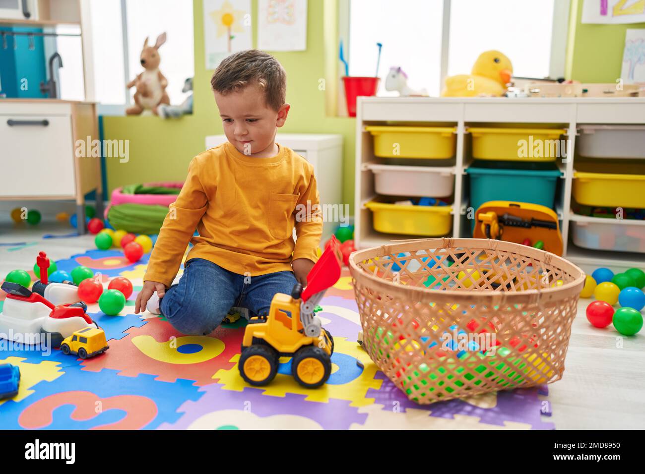 Adorable caucasian boy playing with tractor toy sitting on floor at ...