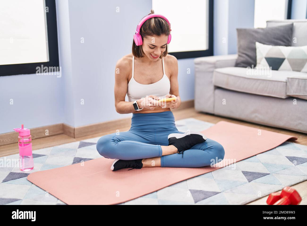 Young beautiful hispanic woman sitting on yoga mat listening to music ...