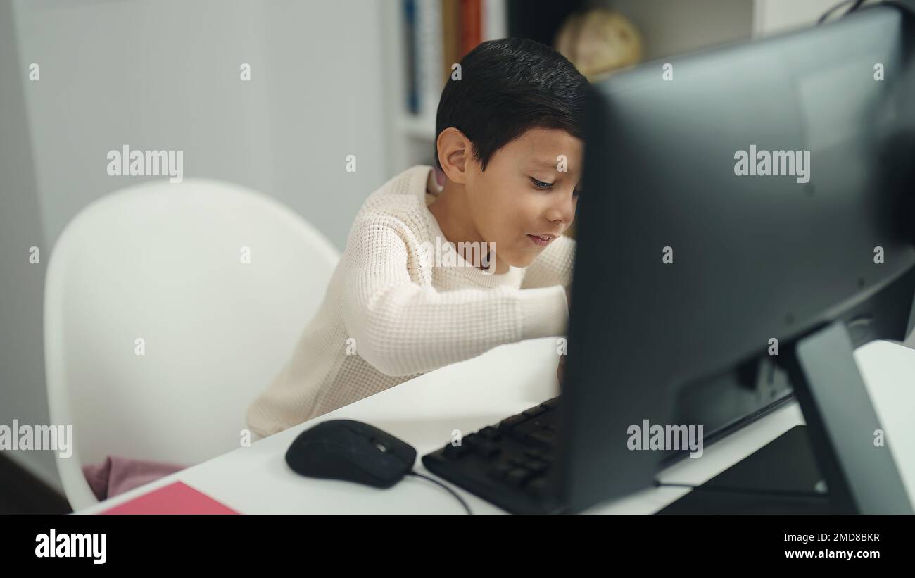 Adorable hispanic boy student using computer sitting on table at ...
