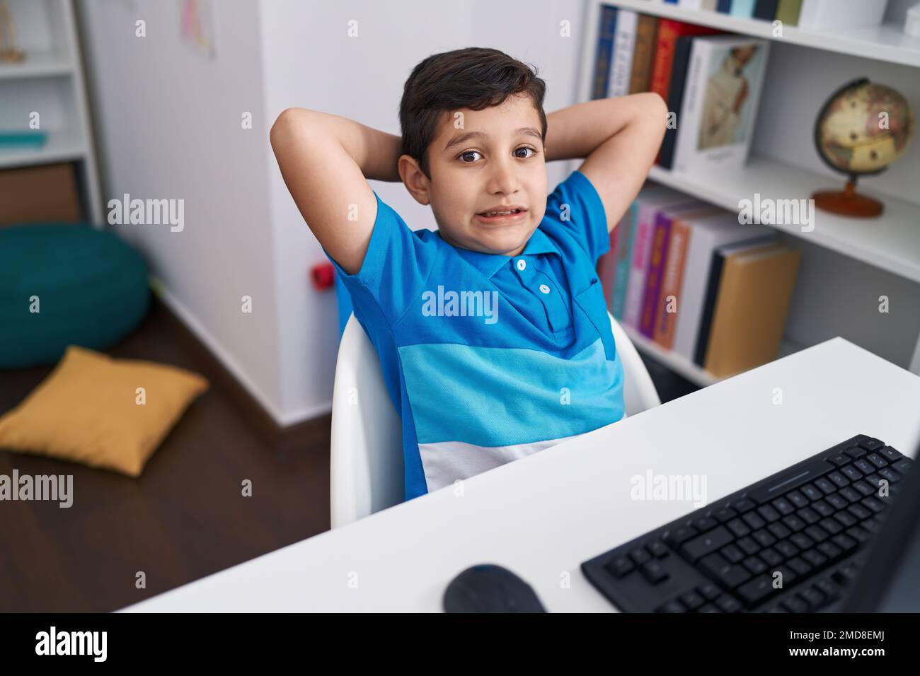 Adorable hispanic boy student using computer relaxed with hands on head ...