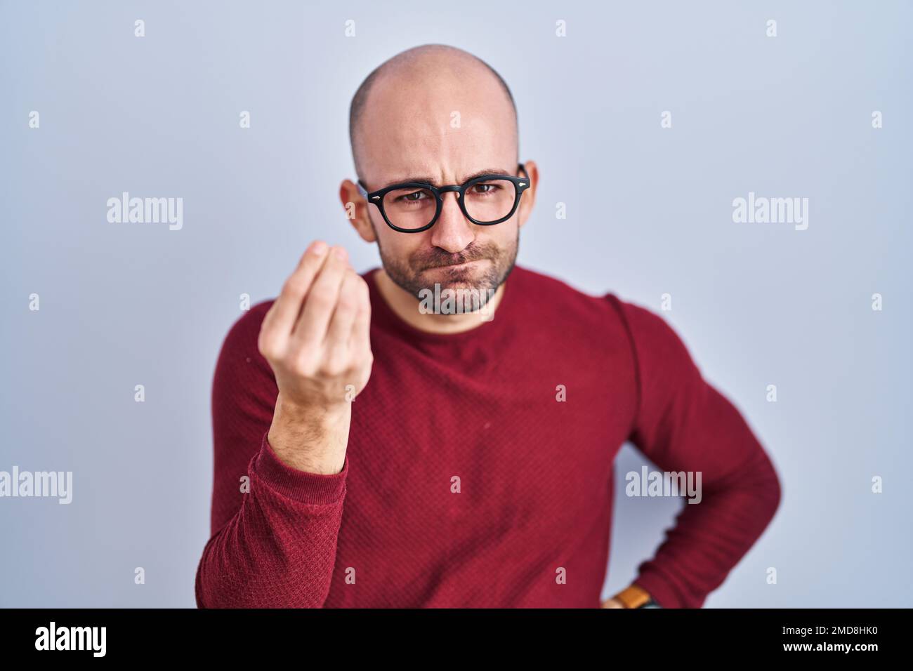 Young bald man with beard standing over white background wearing glasses doing italian gesture with hand and fingers confident expression Stock Photo