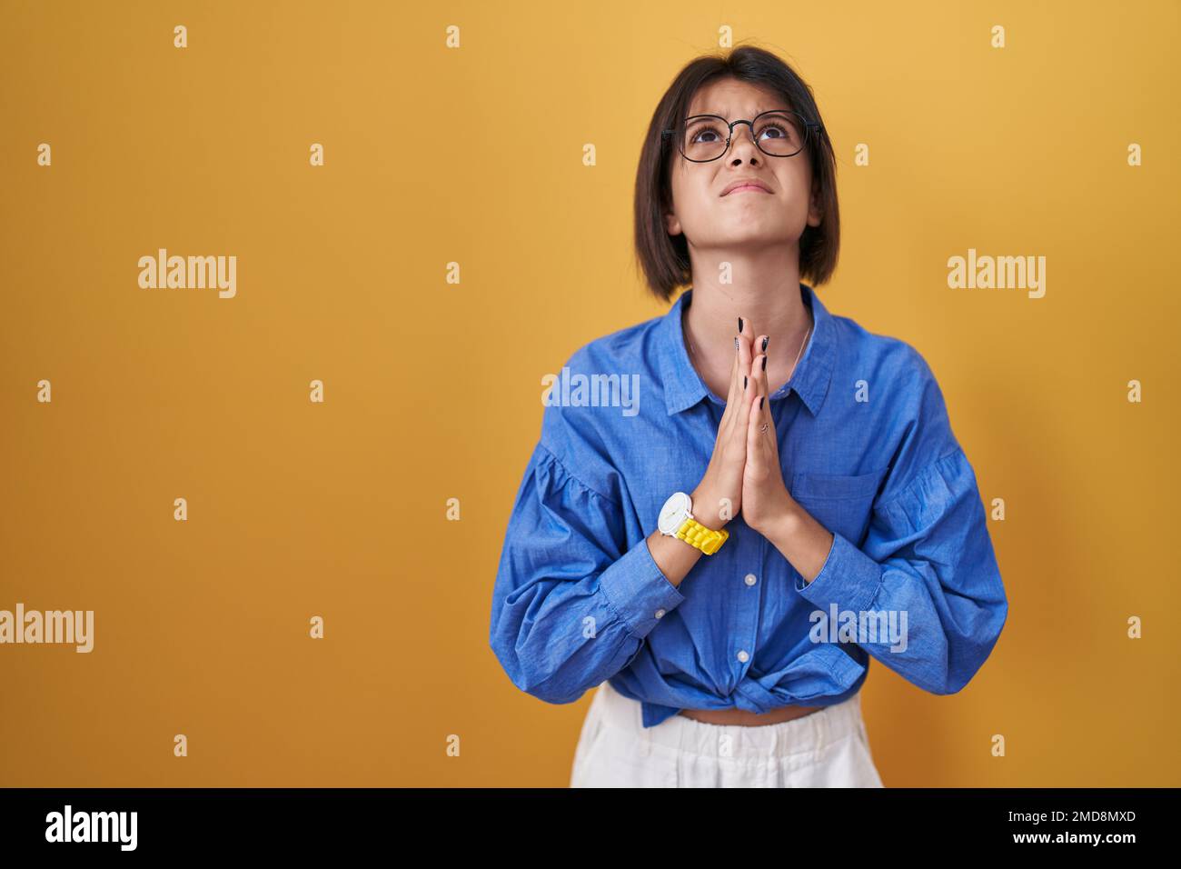 Young girl standing over yellow background begging and praying with ...
