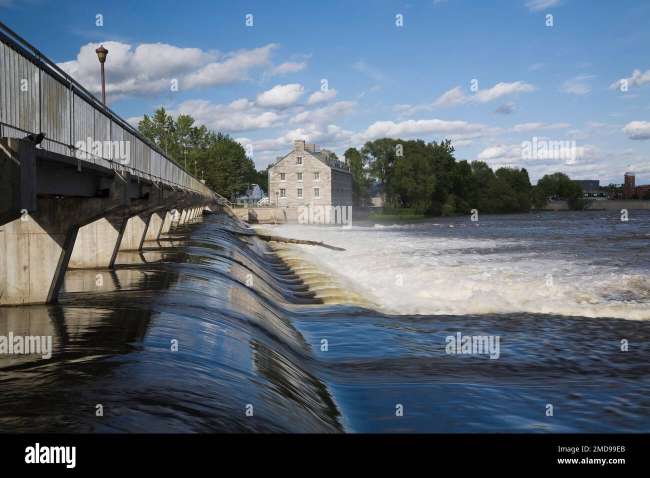 Footbridge and water flow control gate over Des Mille-Iles River and New Mill on Ile des Moulins Historic Site in spring, Old Terrebonne, Quebec. Stock Photo