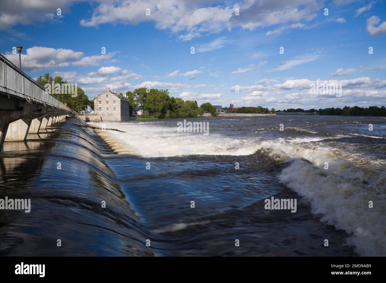 Footbridge and water flow control gate over Des Mille-Iles River and New Mill on Ile des Moulins Historic Site in spring, Old Terrebonne, Quebec. Stock Photo