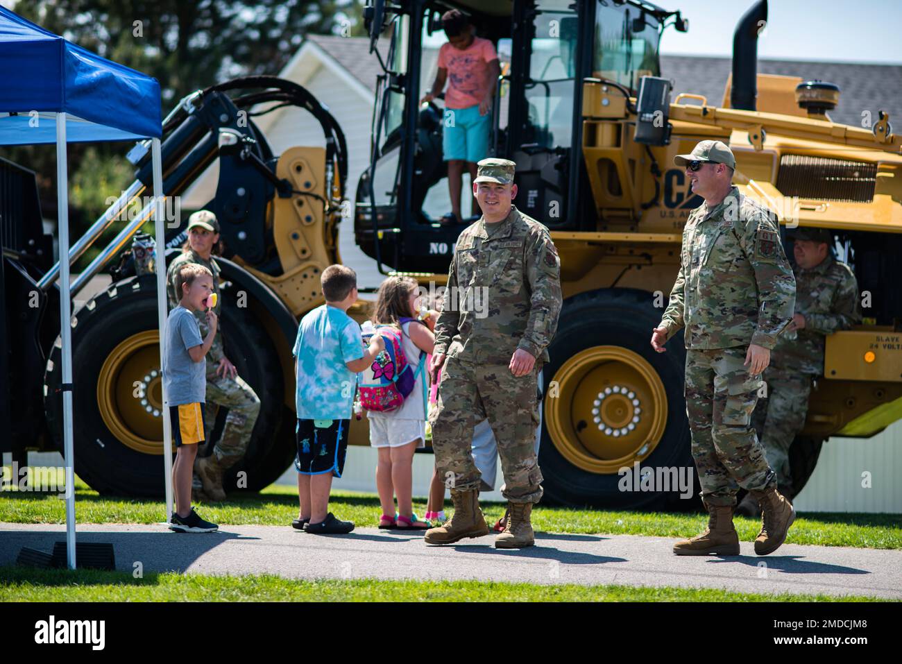Tech. Sgt. Derek Senter, 141st Civil Engineer Squadron and Master Sgt. Evan Jacobus, 141st Logistics Readiness Squadron walk by a front end loader as children wait in line to check it out at Liberty Lake, Wash. July 15, 2022. The Airmen were out supporting the annual Touch-A-Truck event allowing both children and adults to check out heavy equipment from multiple agencies. Stock Photo